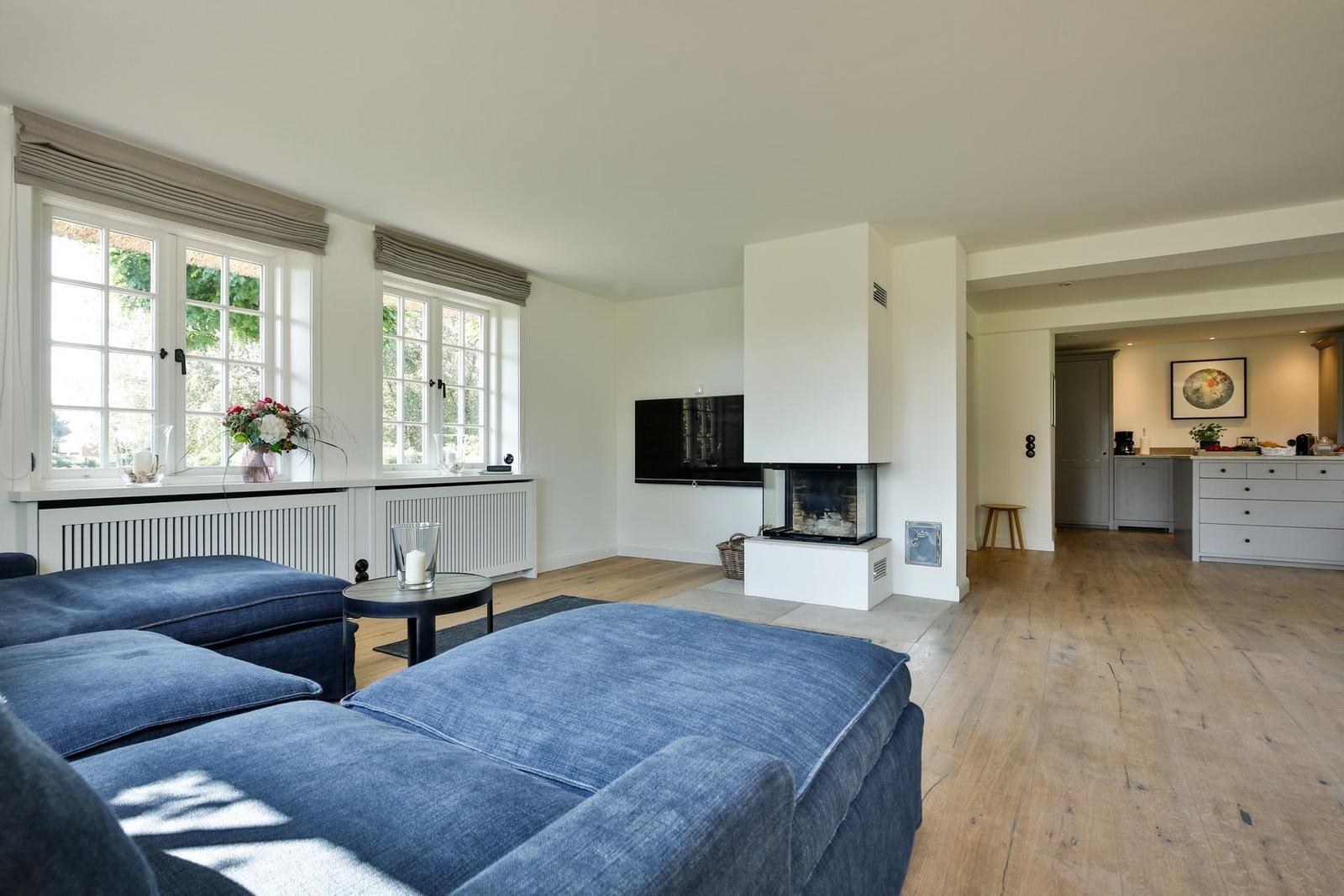 Living room with blue sofa, fireplace, and wooden floor. Kitchen in the background.