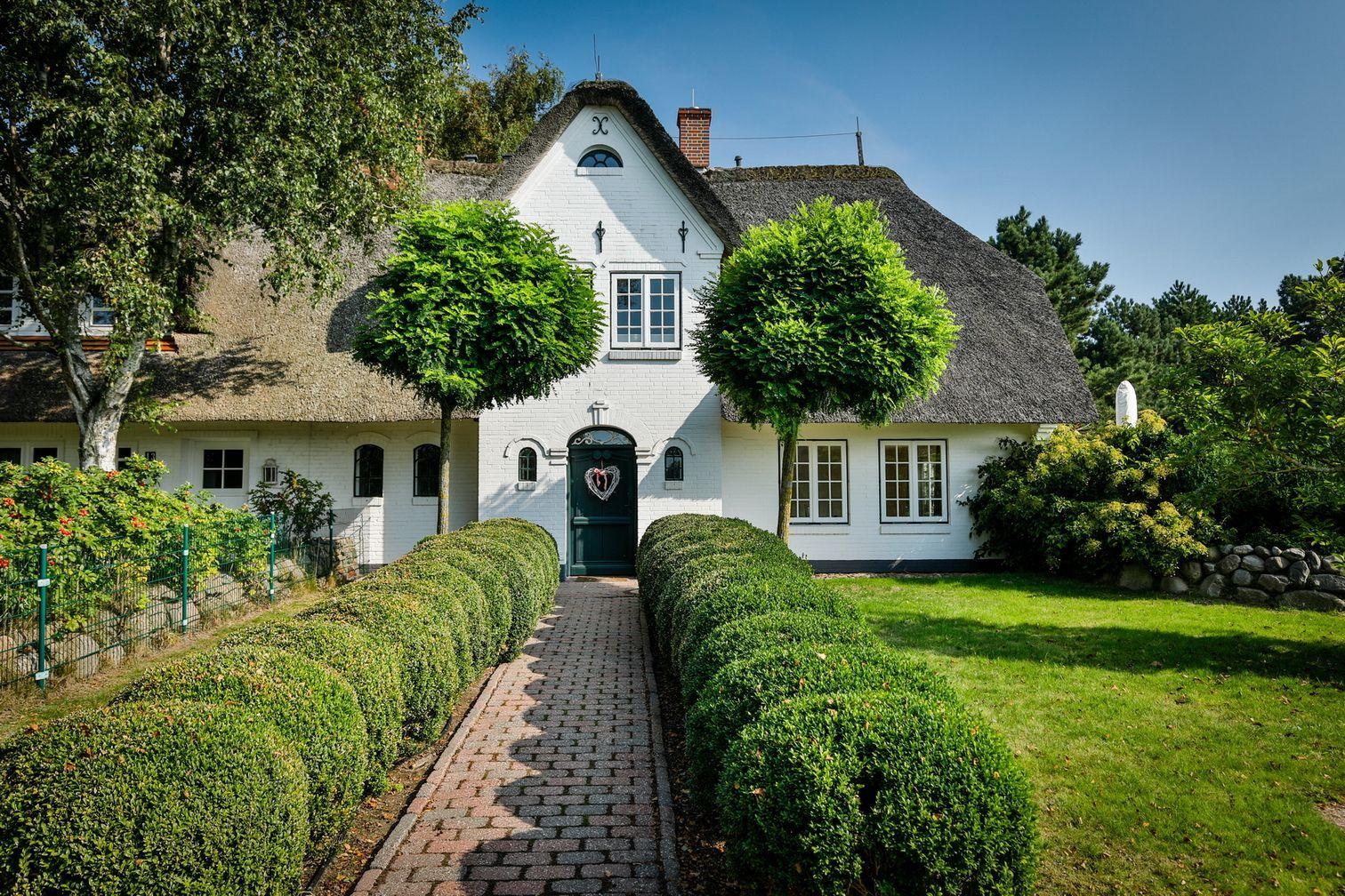White cottage with thatched roof, manicured garden, and gravel path to the entrance door.