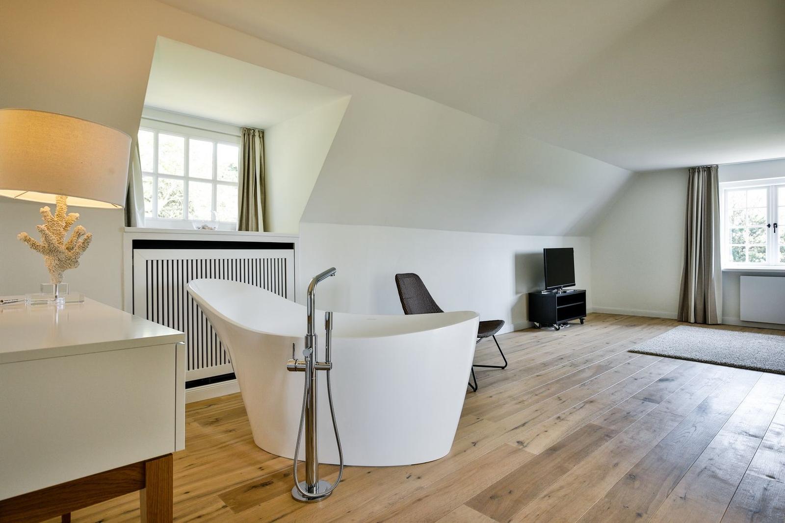 Attic room with freestanding bathtub, wooden floor, and windows.