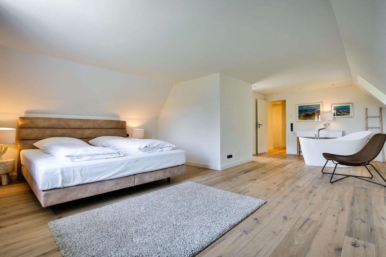 Bedroom with bed, rug, and bathroom. Wooden floor and white walls.