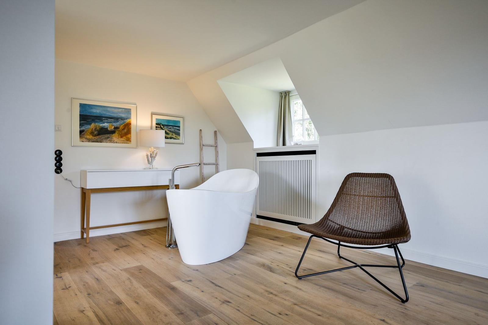 Attic room with freestanding bathtub, chair, and window.