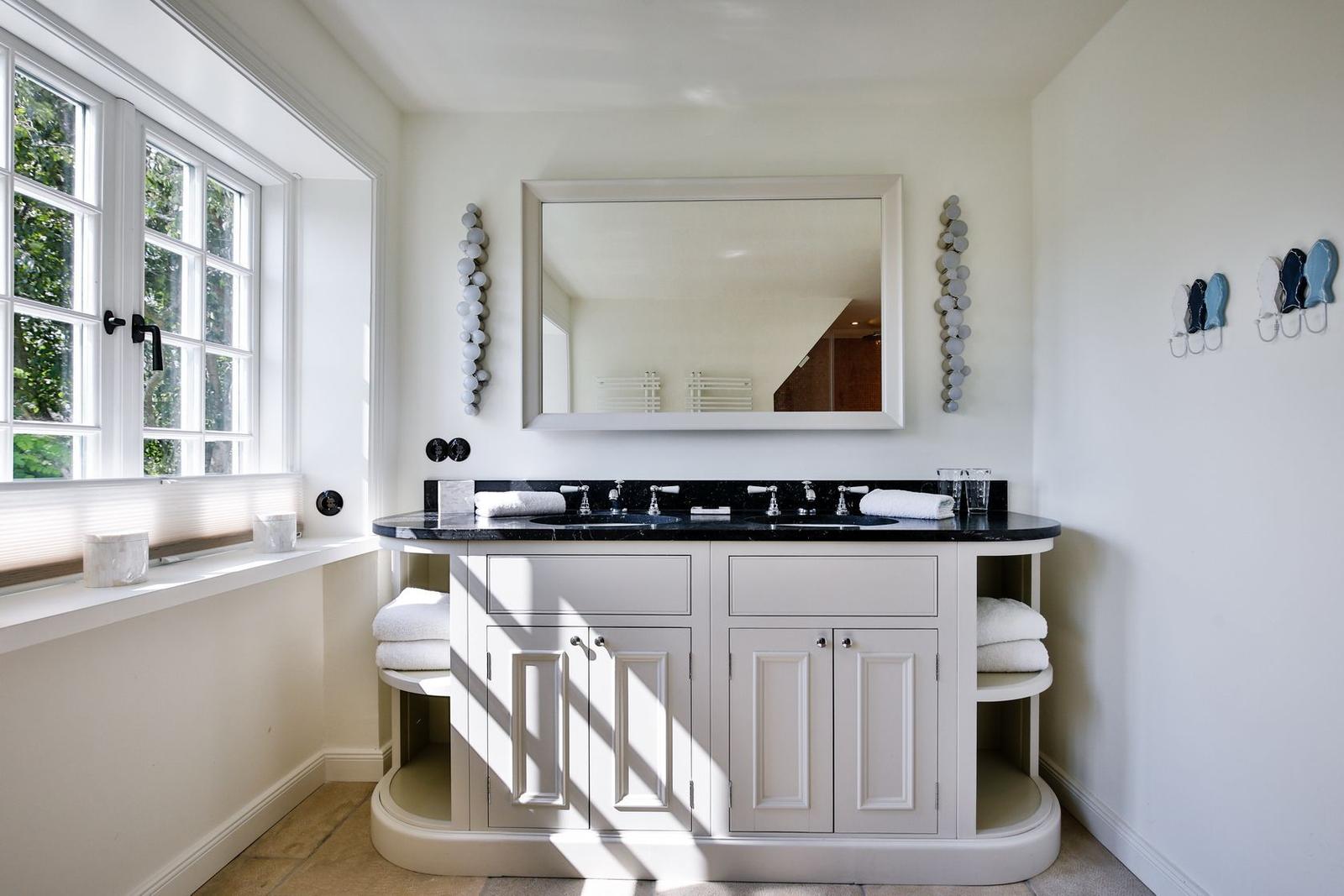 Bathroom with sink, mirror, and window. White furniture and black countertop.
