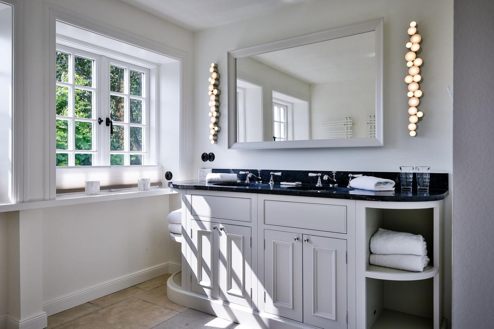 Bathroom with white vanity, mirror, and window overlooking trees.