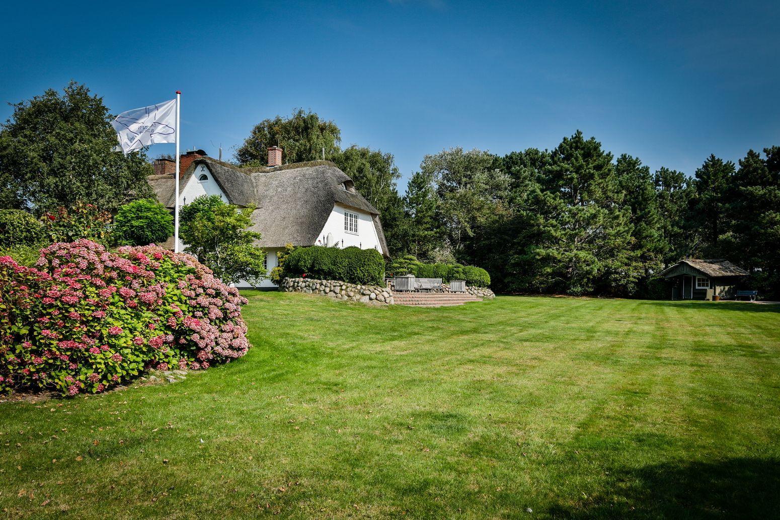 A white house with thatched roof, surrounded by grass and flowers.