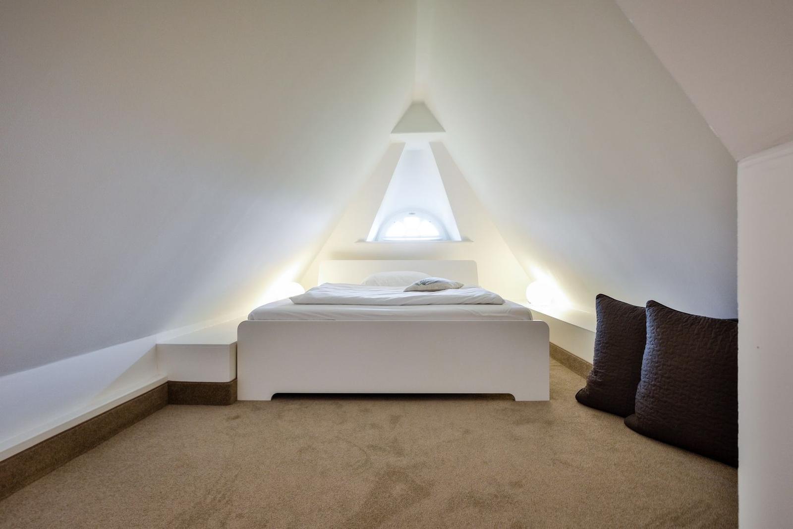 Bedroom with sloped ceiling, white bed, and window
