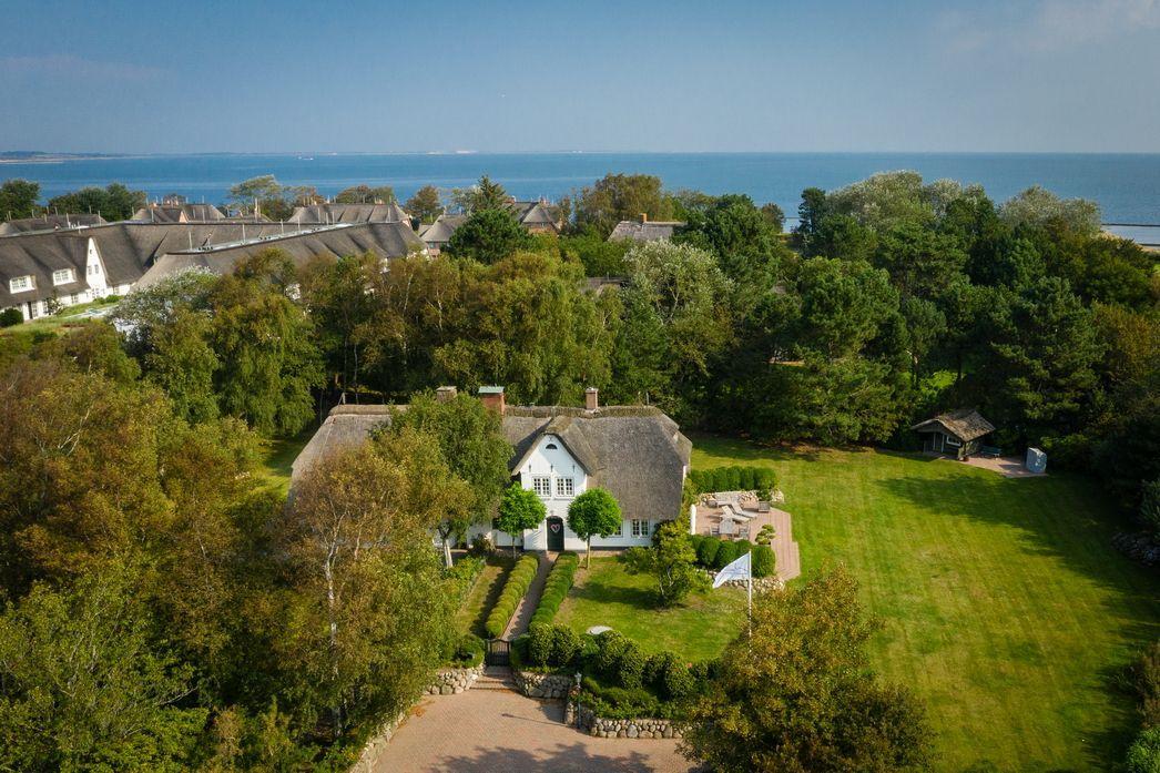 House with thatched roof, surrounded by greenery and trees, view of the sea.
