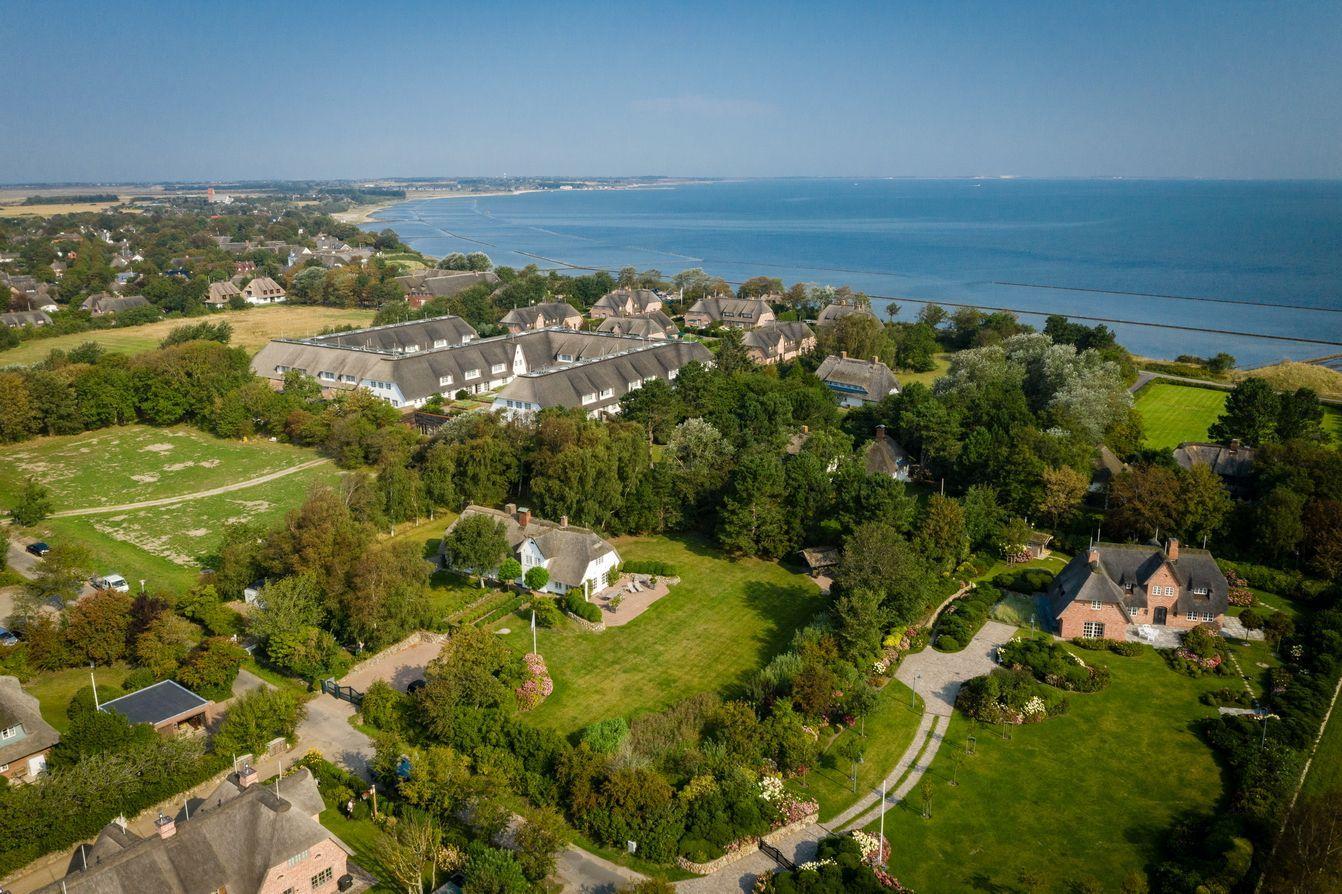 Aerial view of holiday homes by the sea with green gardens and trees.