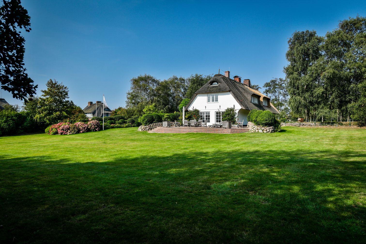 House with thatched roof and large garden with terrace.