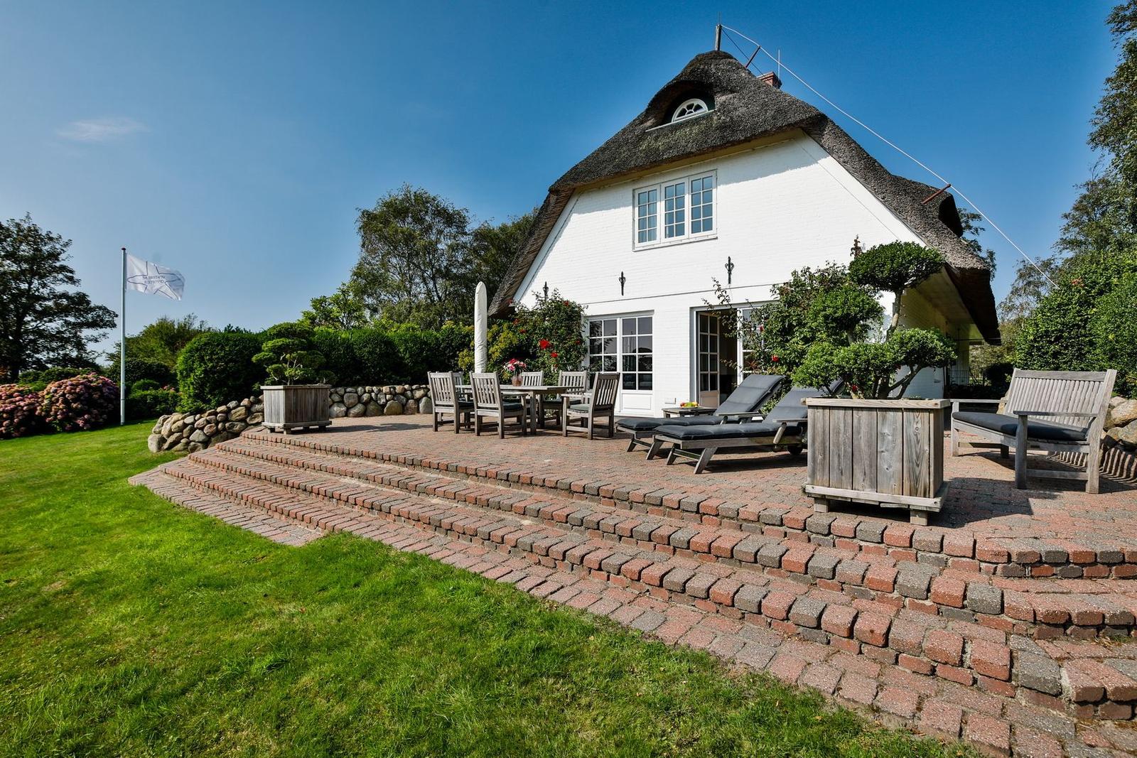 House with thatched roof and terrace with loungers and table.