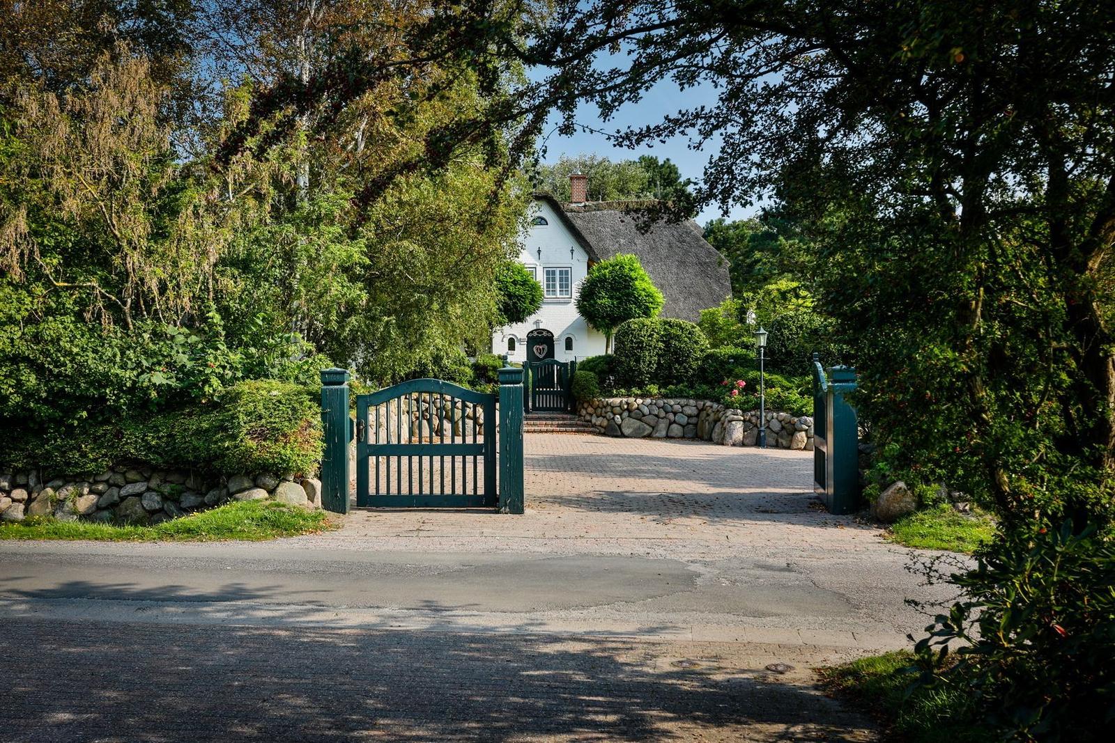 A white house with a thatched roof behind a green gate and stone walls.