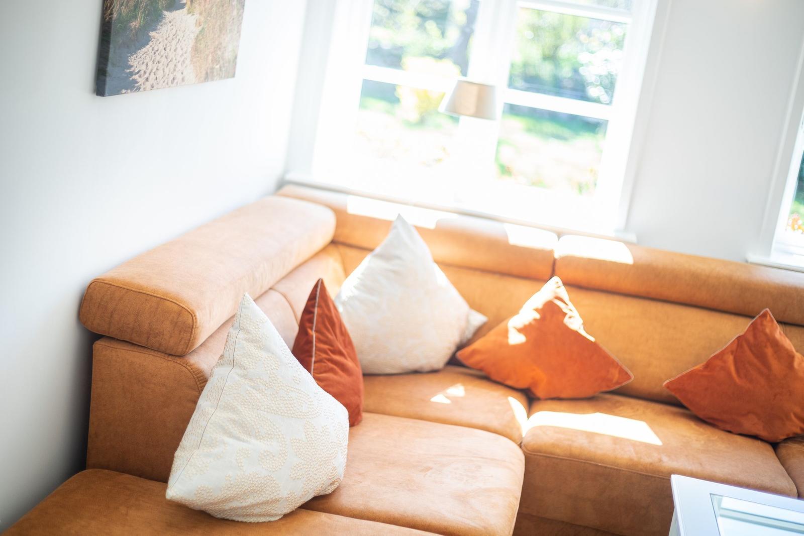 Ein braunes Sofa mit Kissen in Orange und Weiß vor einem Fenster.