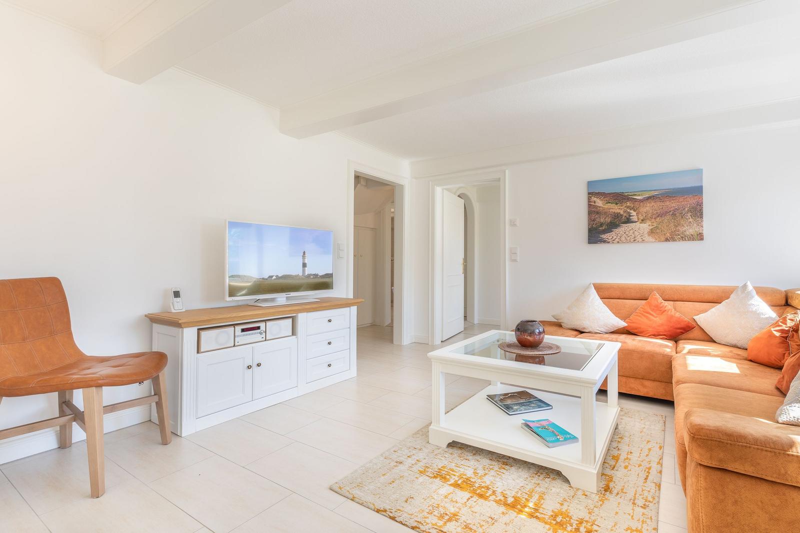 Wohnzimmer mit orangefarbenem Sofa, Fernseher und Glas-Tisch.
