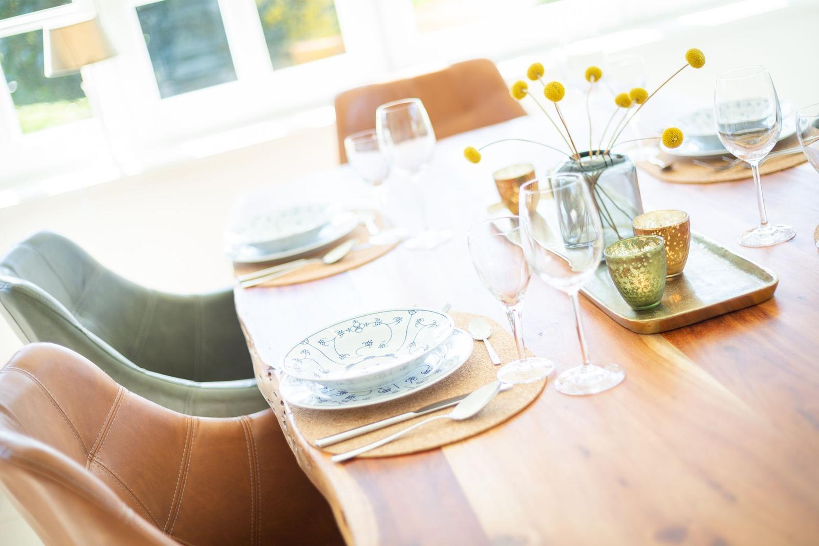 Esstisch mit Stühlen, Teller, Gläsern und Blumenarrangement.
