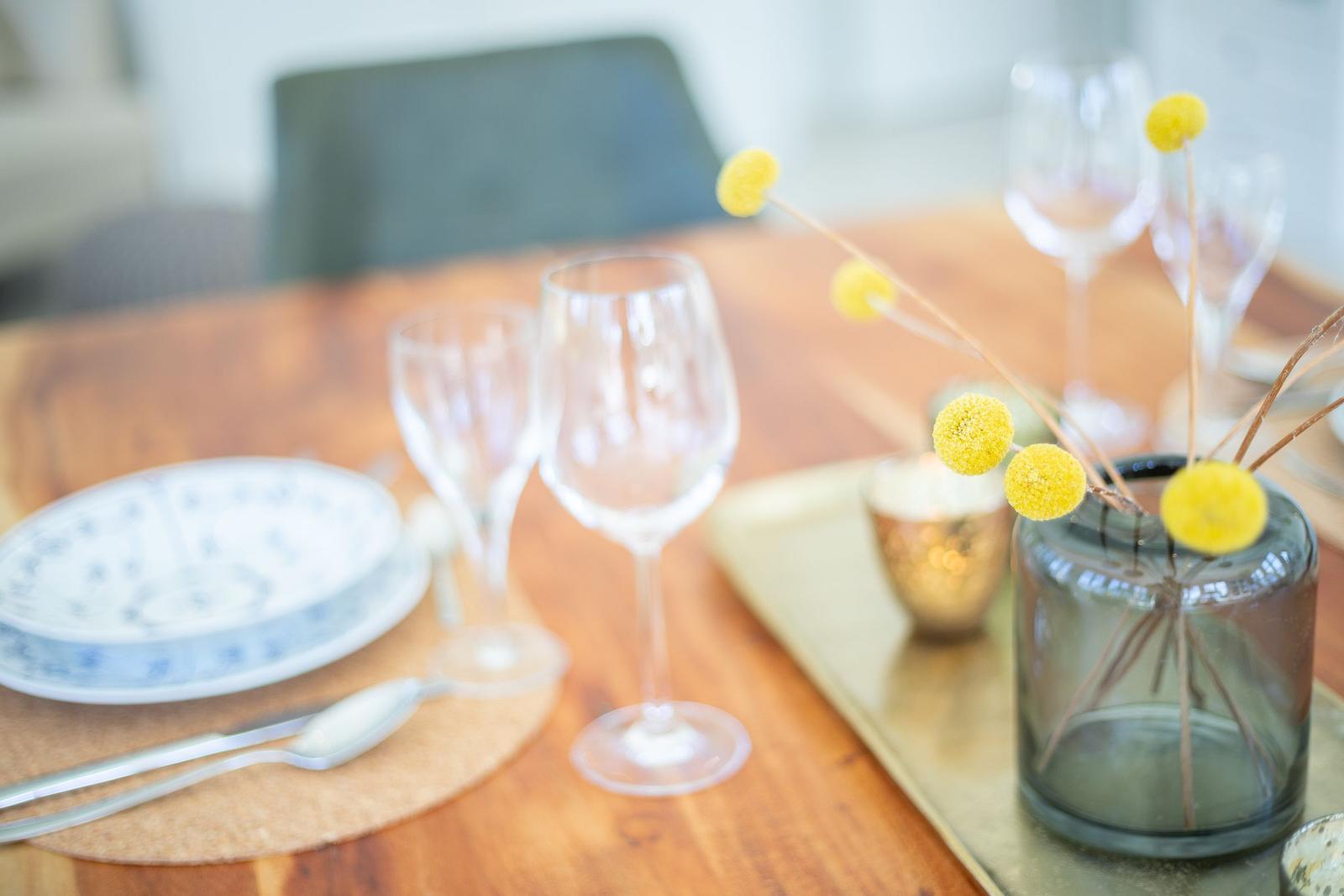 Holztisch mit Geschirr, Gläsern und gelben Blumen in einem Glas.