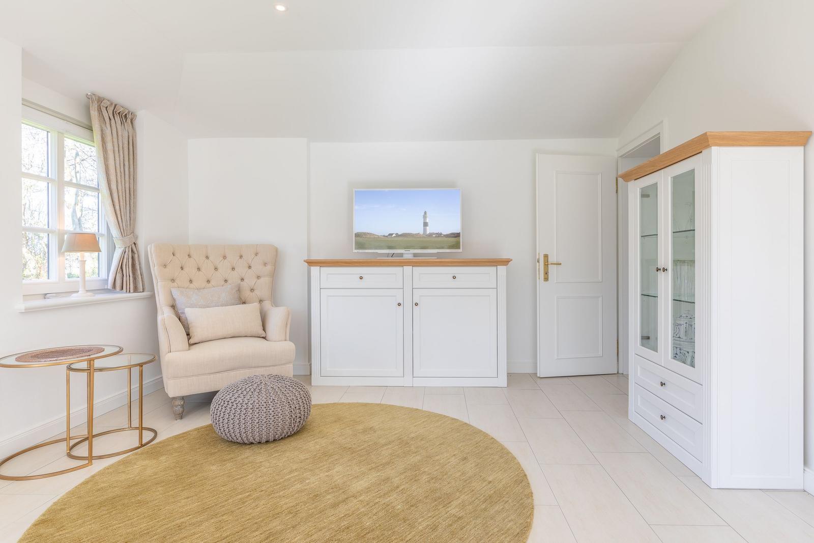 Ein Wohnzimmer mit Sessel, Fernseher und Schrank. Fenster und Teppich sind sichtbar.