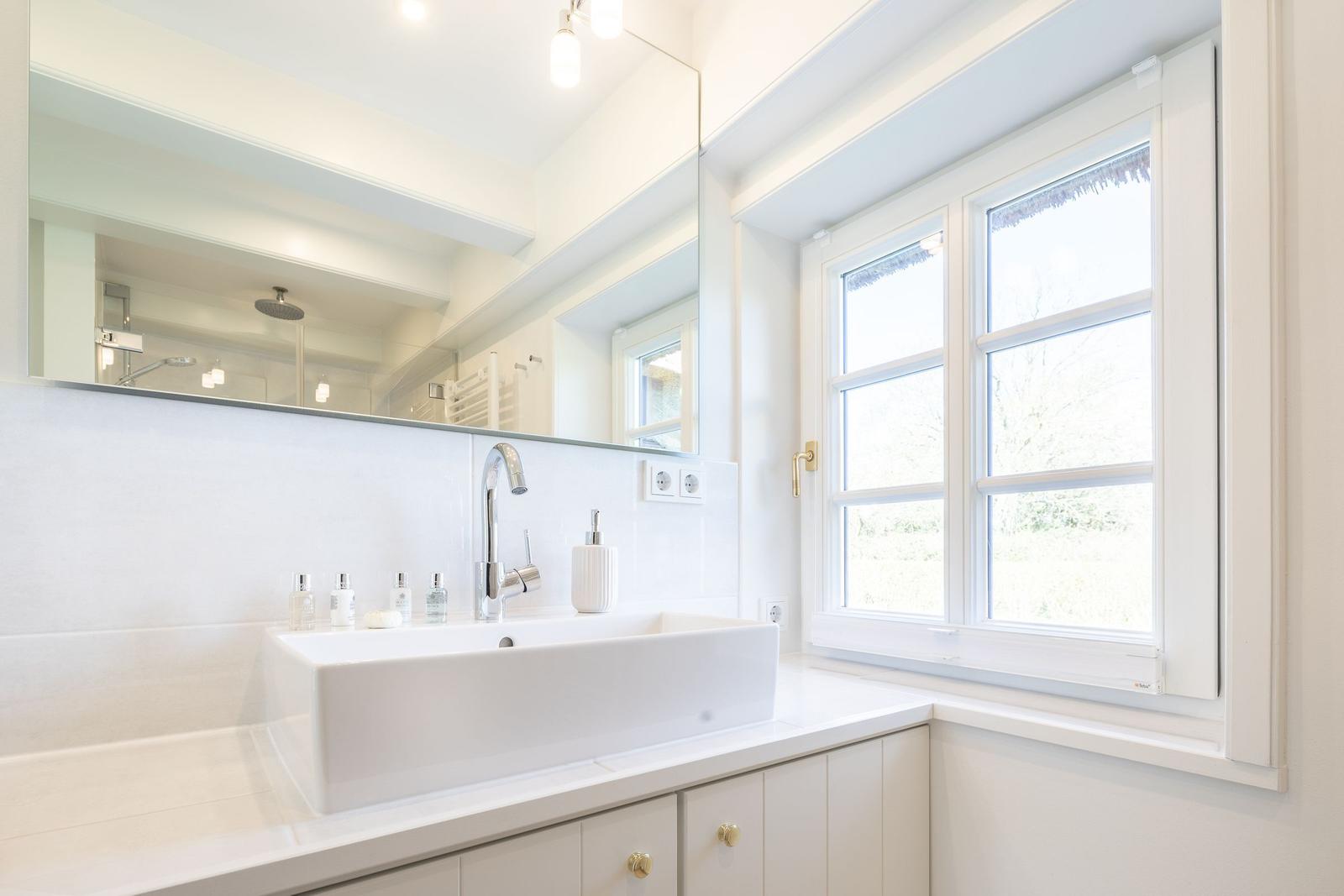 Badezimmer mit Waschbecken, Spiegel und Fenster