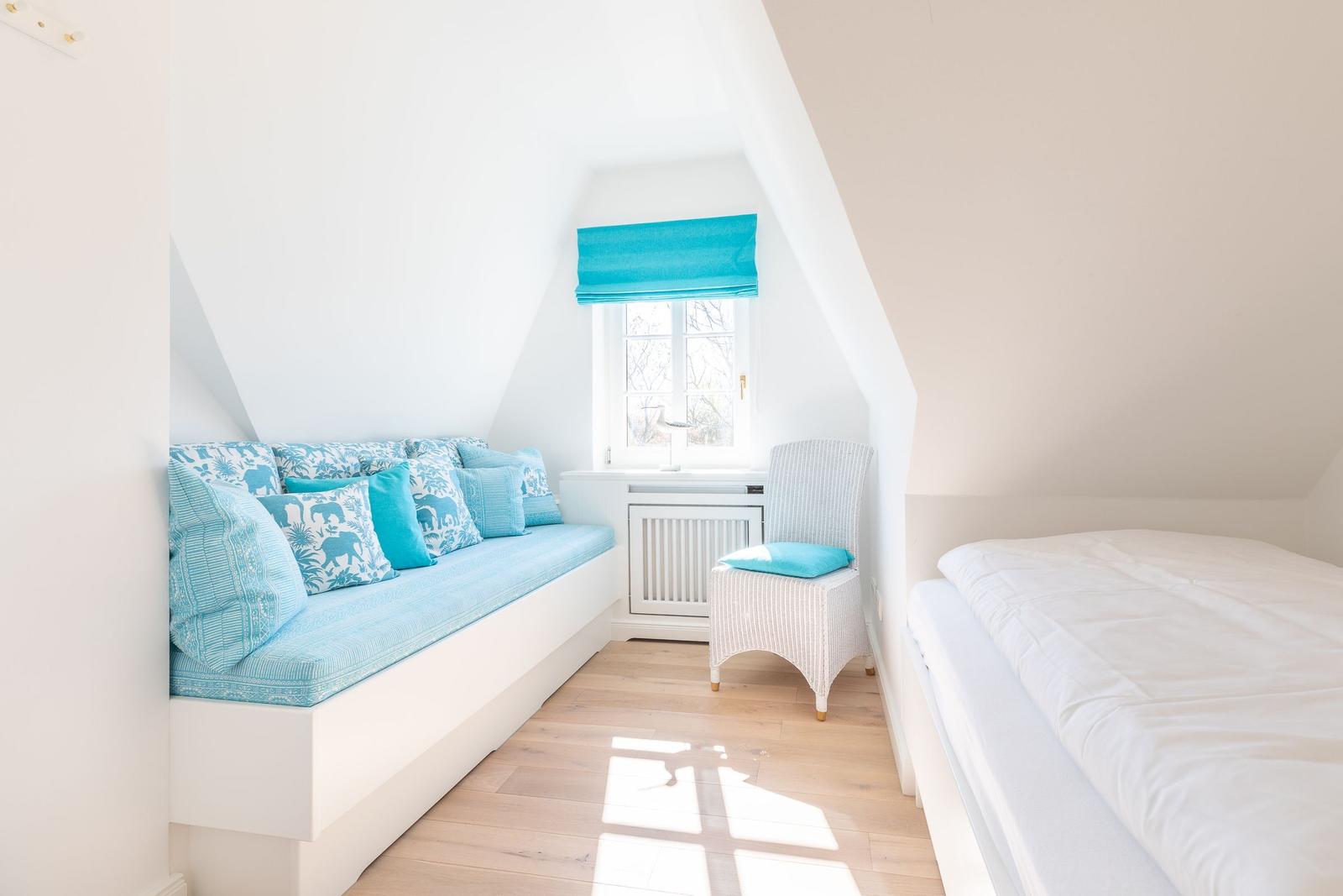 Ein Schlafzimmer mit Bett, Sitzbank und Fenster unter Dachschräge.