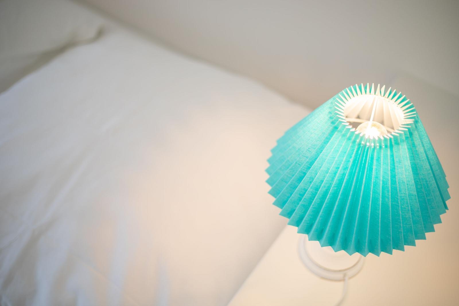 Eine blaue Lampe neben einem Bett mit weißer Bettwäsche.
