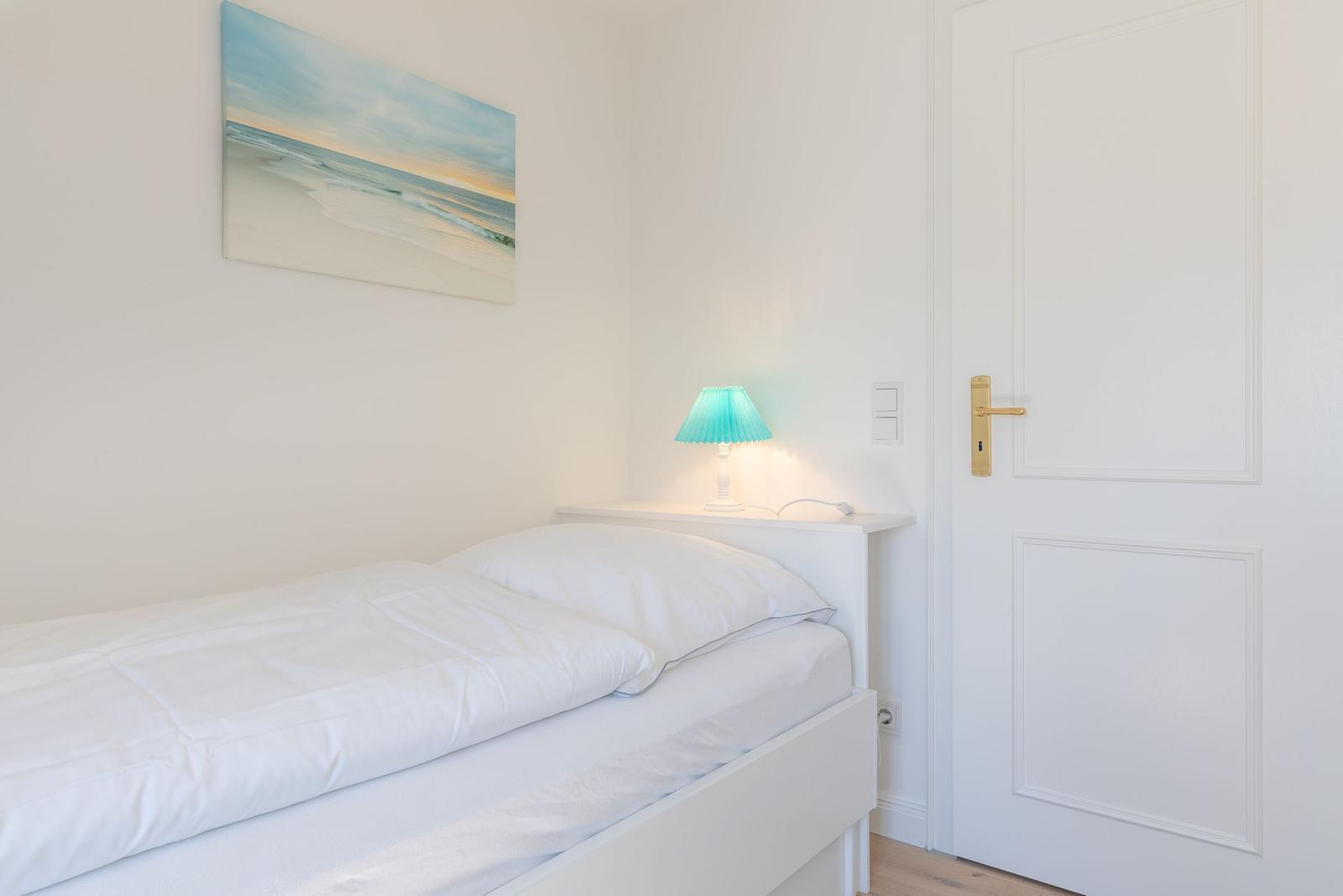 Schlafzimmer mit weißem Bett, Wandbild und Lampe.