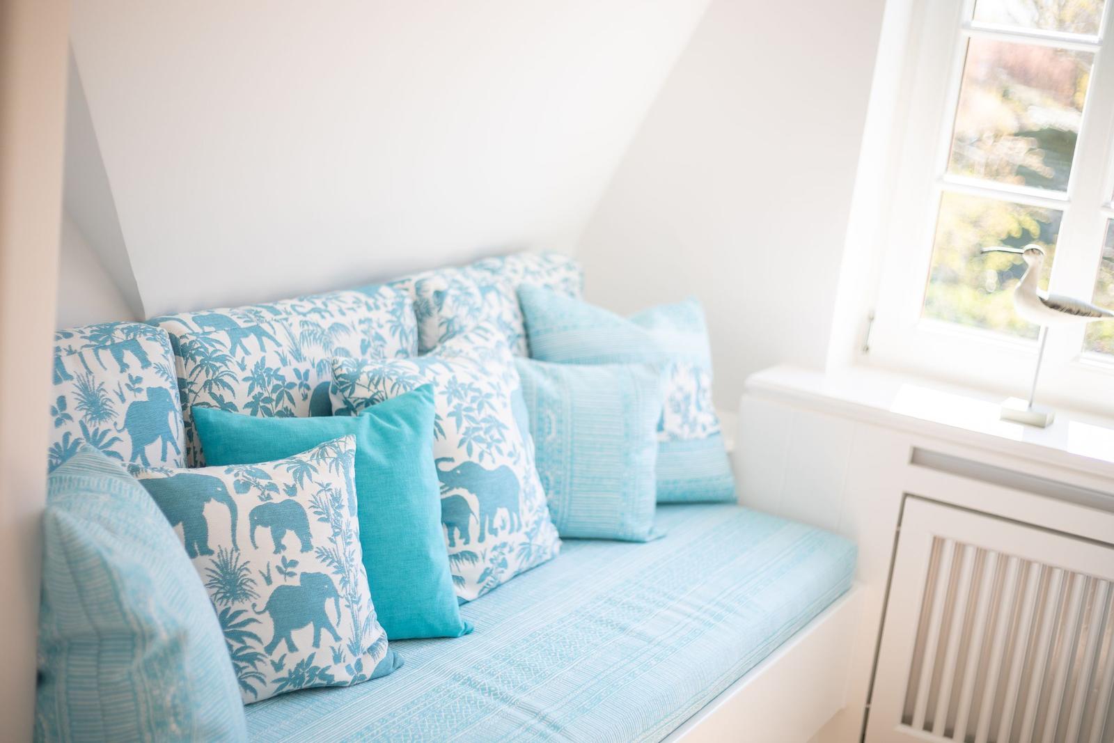Sitzbank mit blauen Kissen und Elefantenmuster unter Fenster