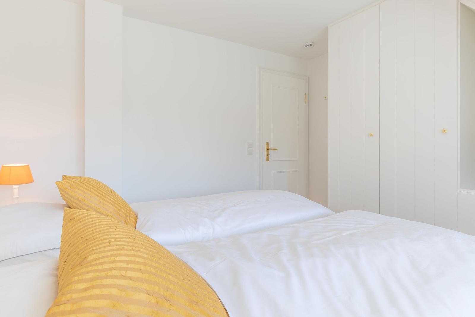 Schlafzimmer mit weißem Bett, gelben Kissen und Schrank
