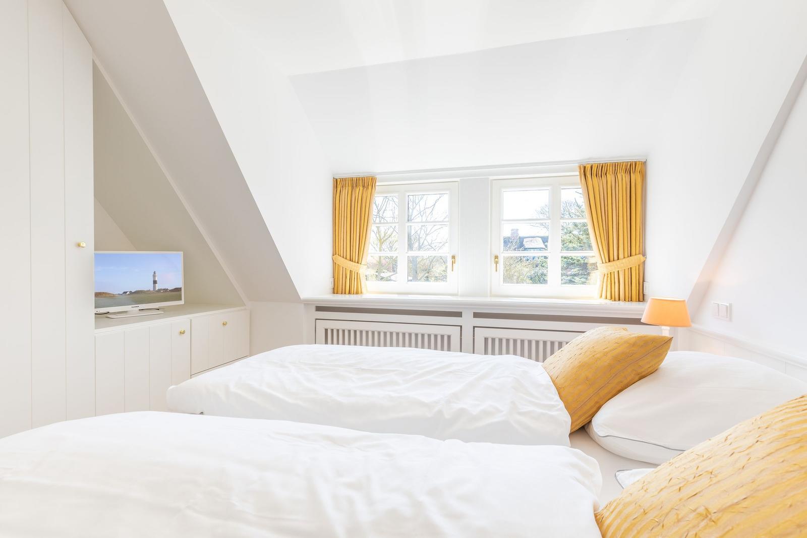 Zimmer mit Dachschrägen, Fenster und Bett mit gelben Kissen.