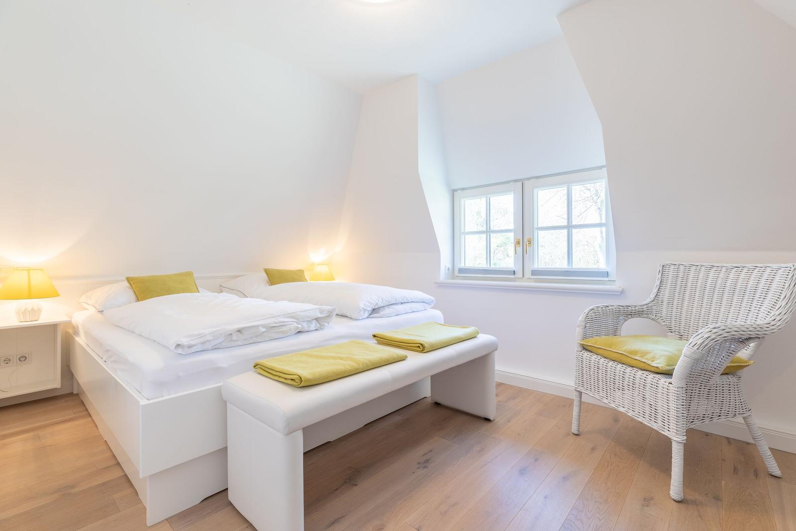 Schlafzimmer mit Doppelbett, Sitzbank und Stuhl. Fenster mit Blick nach draußen.