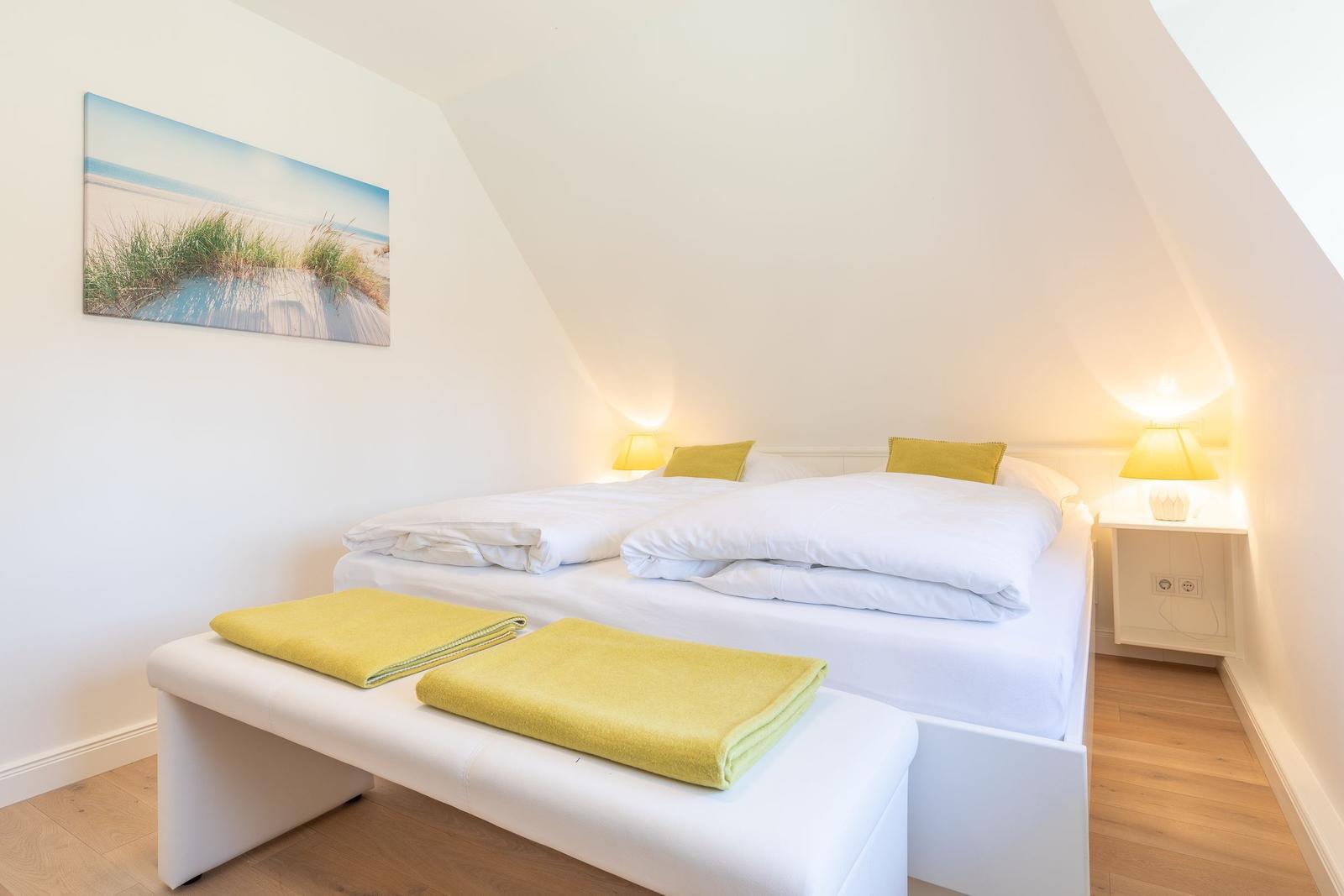 Schlafzimmer mit Doppelbett, gelben Kissen und Handtüchern, Wandbild und Nachttischen.