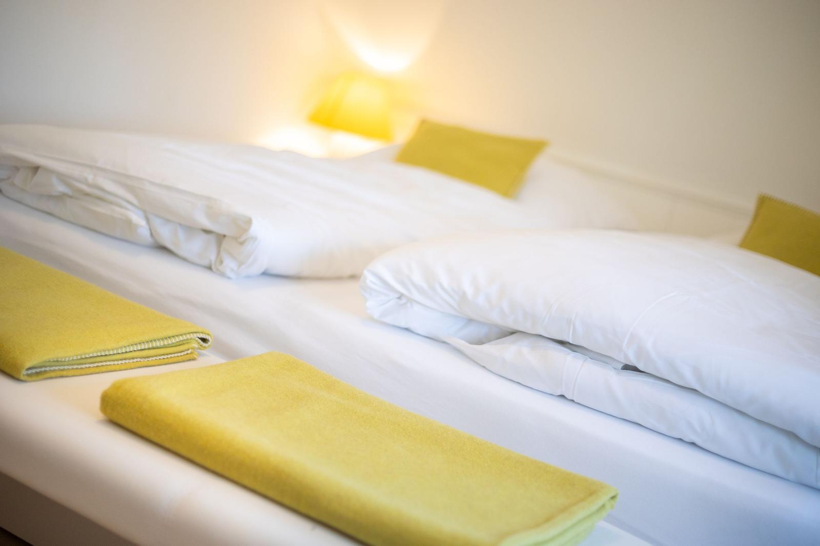 Ein Bett mit weißen Laken und zwei gelben Kissen. Zwei gelbe Handtücher liegen auf dem Bett.