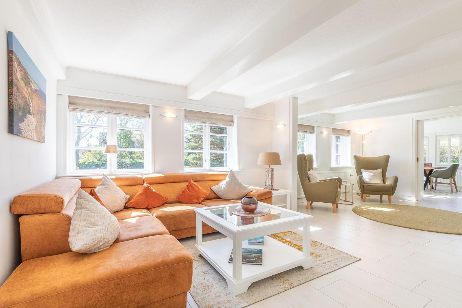 Wohnzimmer mit orangefarbenem Sofa, Glas-Tisch und zwei Sesseln.
