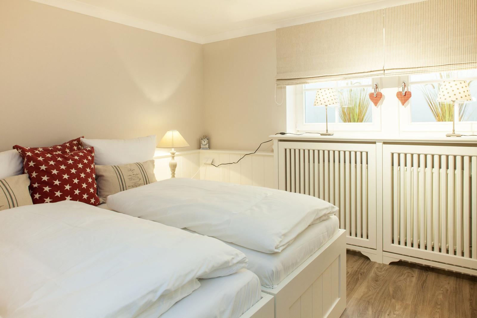 Room with two beds, window with roller blind and lamp on windowsill.