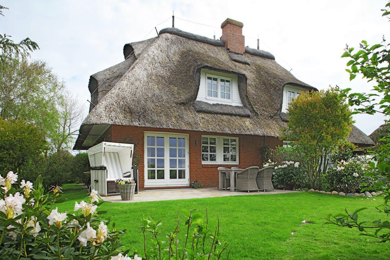 House with thatched roof, terrace, and garden with seating.