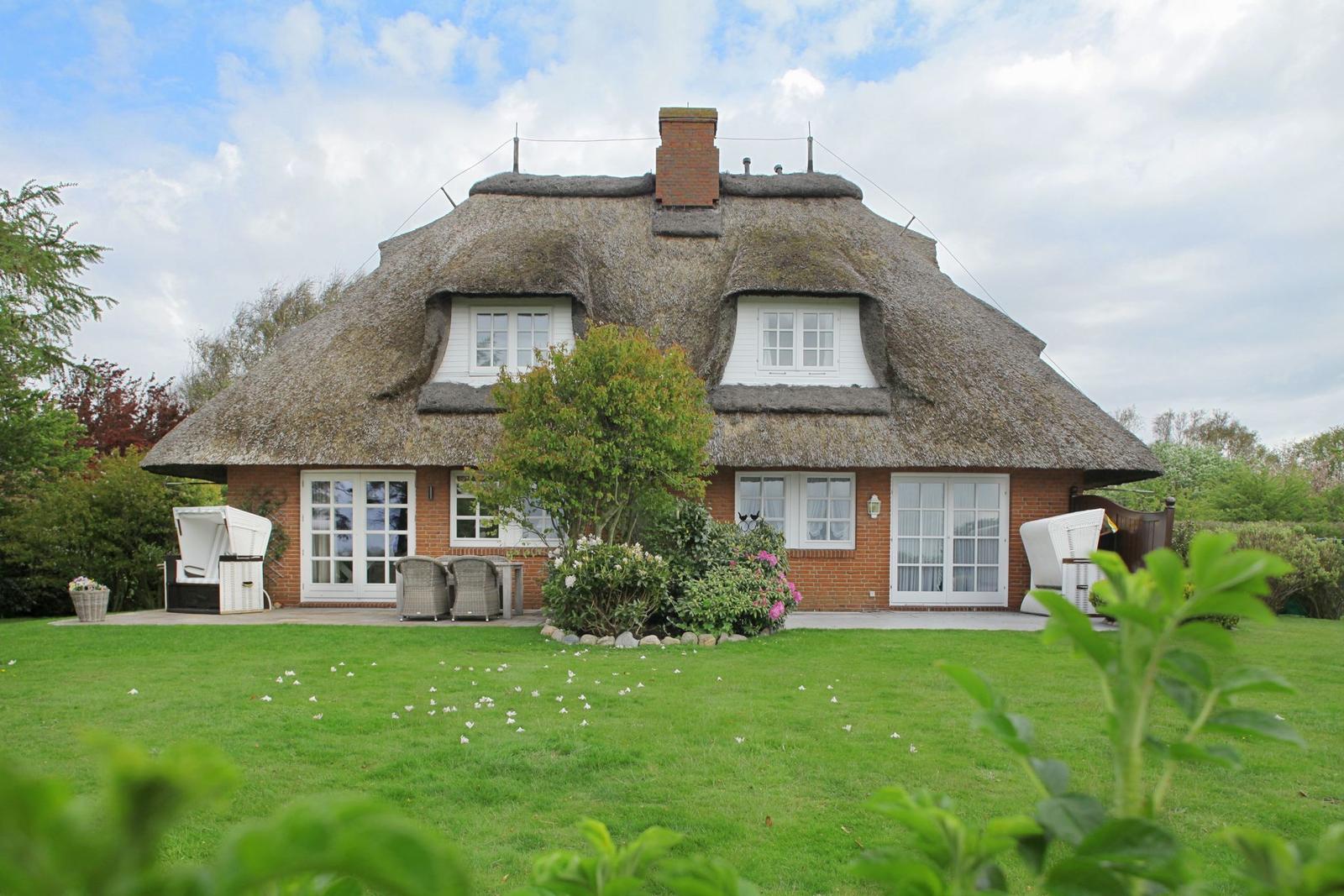 House with thatched roof, white-framed windows, and garden with seating.