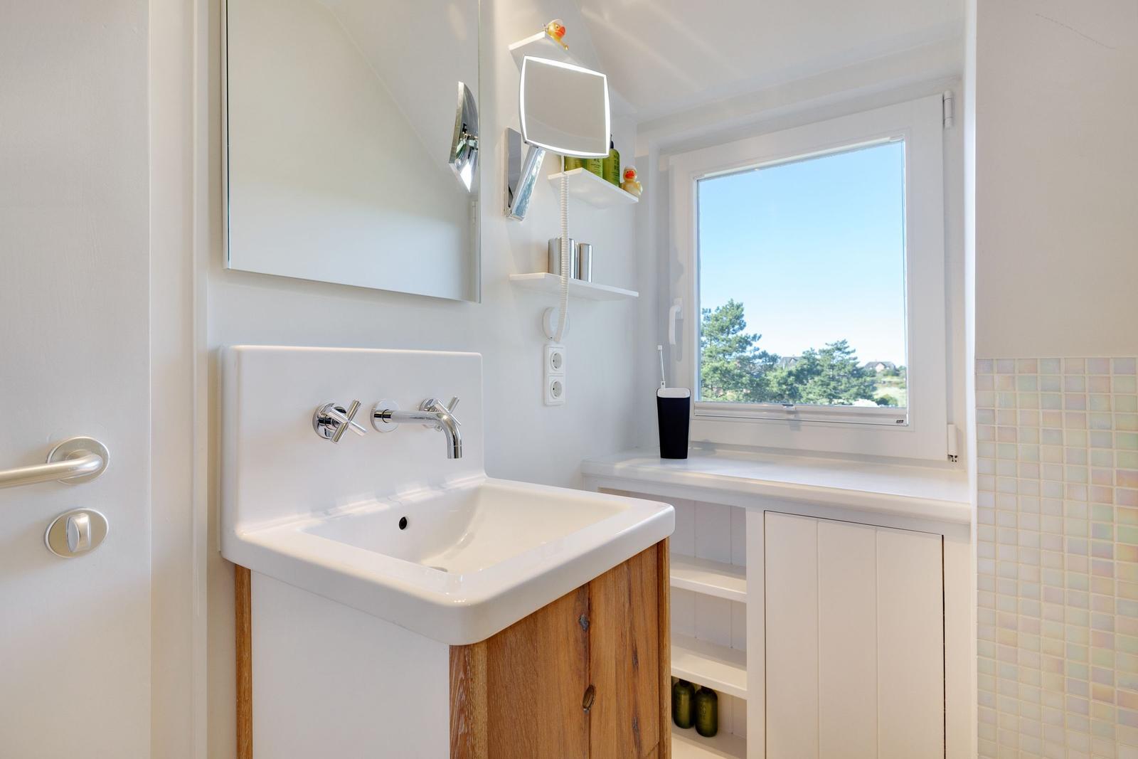 Badezimmer mit Waschbecken, Spiegel und Fenster mit Blick auf Bäume.