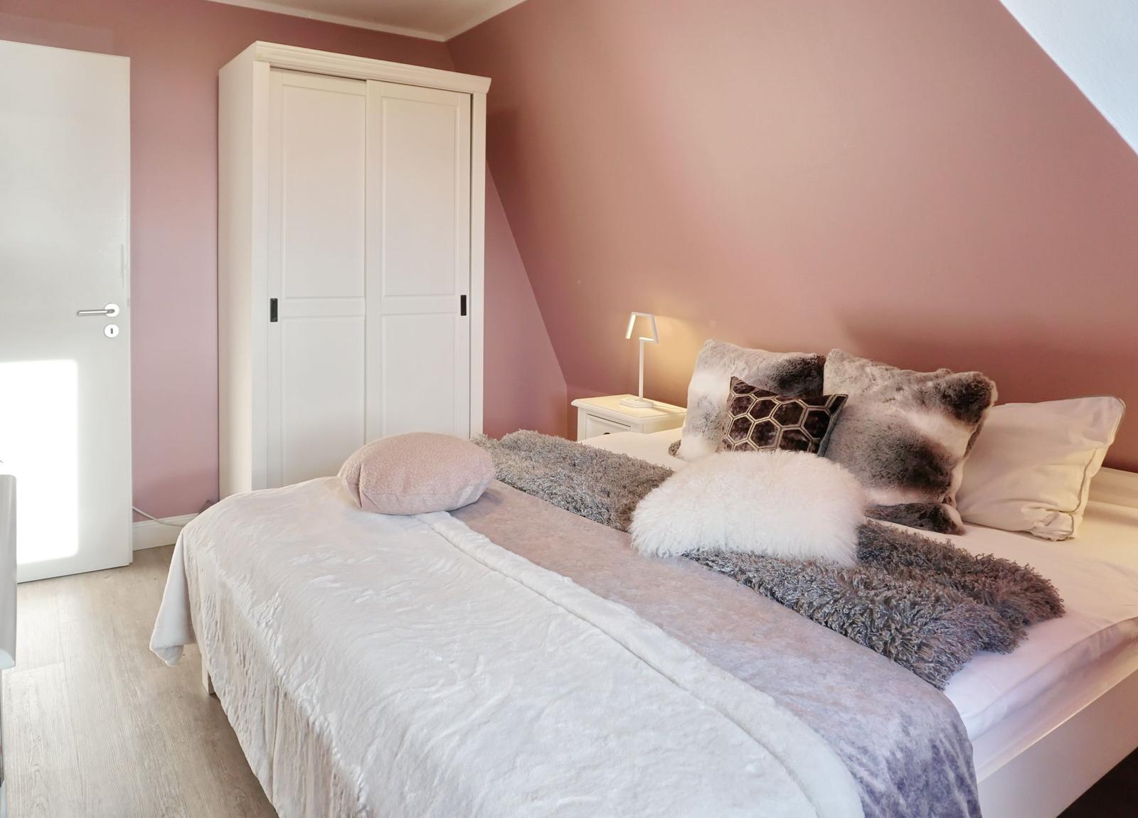 Schlafzimmer mit Bett, Schrank und Nachttisch. Wände rosa, Boden hell.