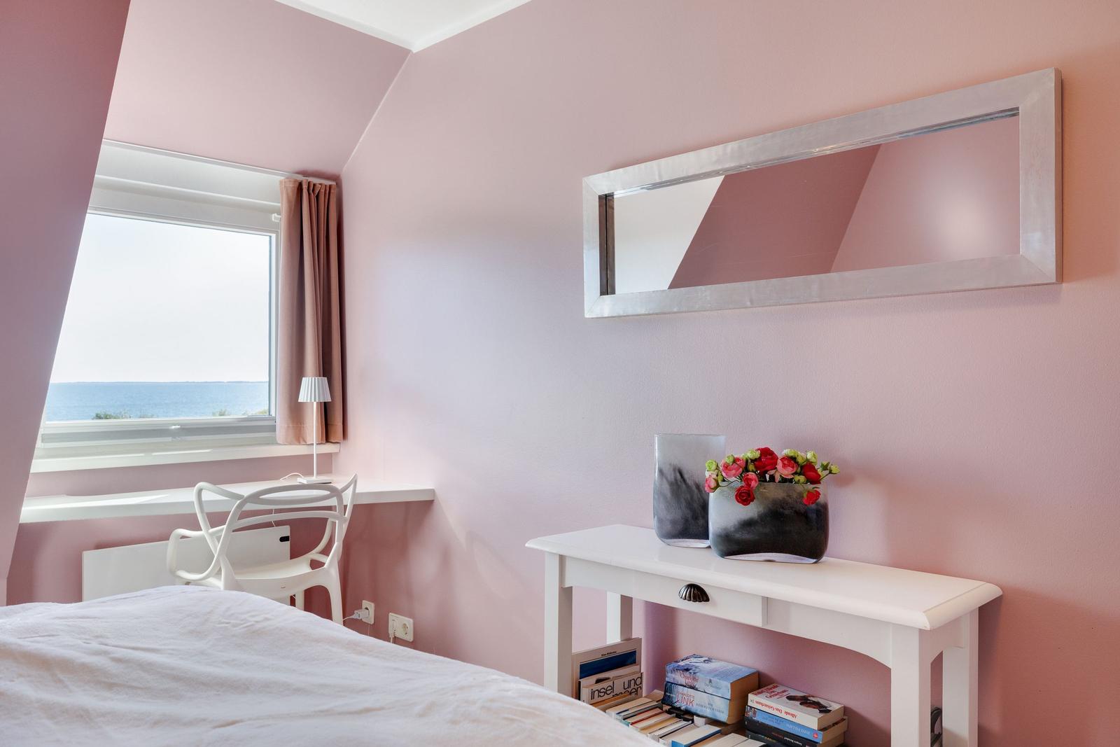 Schlafzimmer mit Blick aufs Meer, rosa Wände, Spiegel und Schreibtisch.