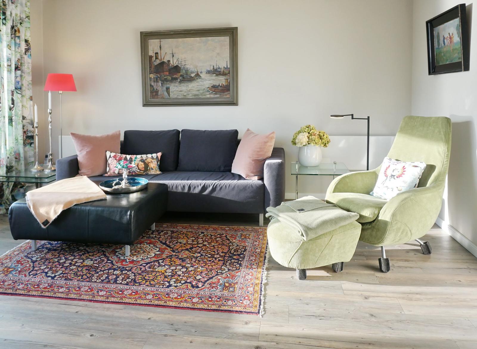Ein Wohnzimmer mit Sofa, Sessel, Teppich und Wandbild.