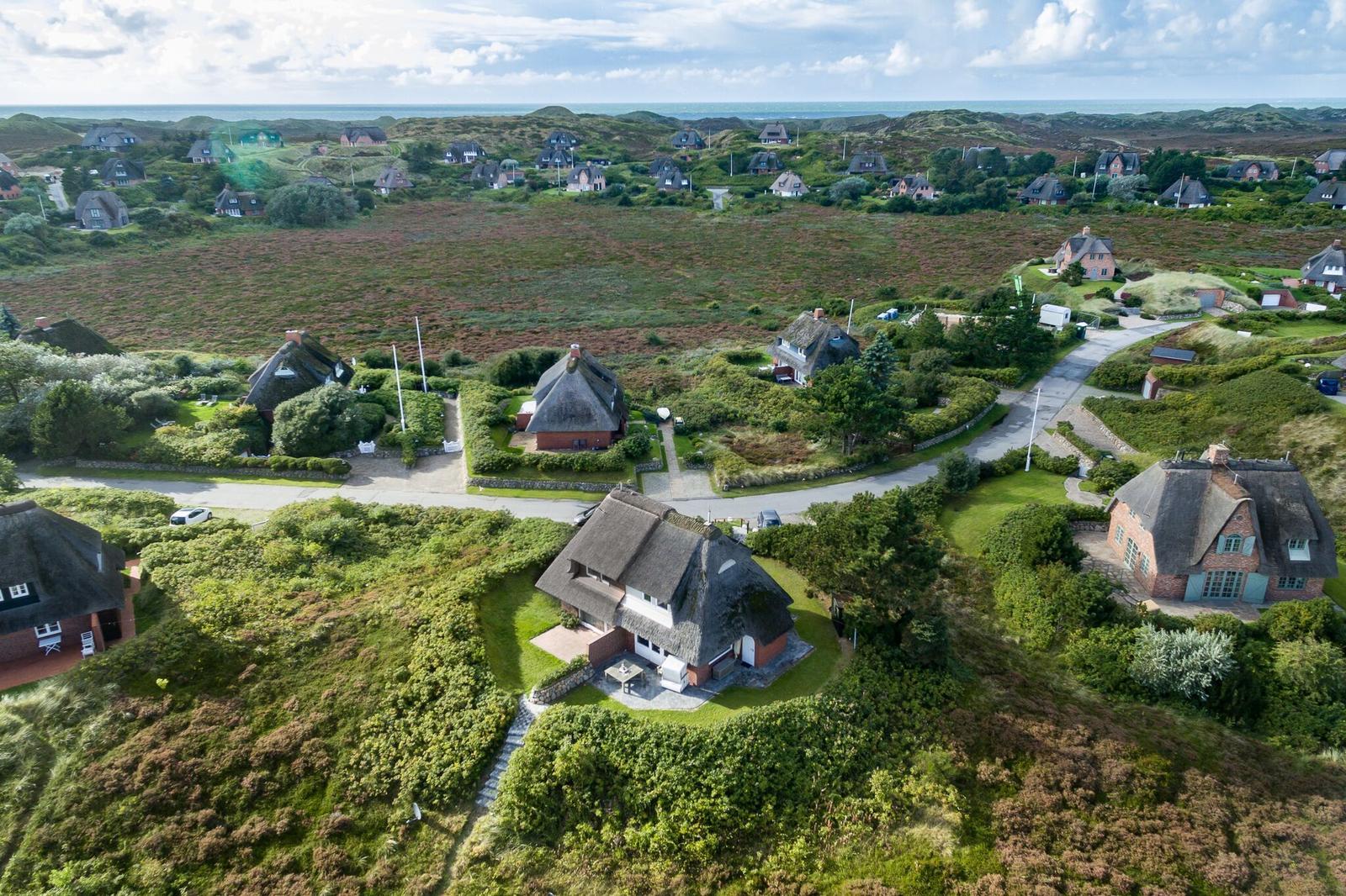 Dorf mit strohgedeckten Häusern und grünen Hängen. Blick aufs Meer.