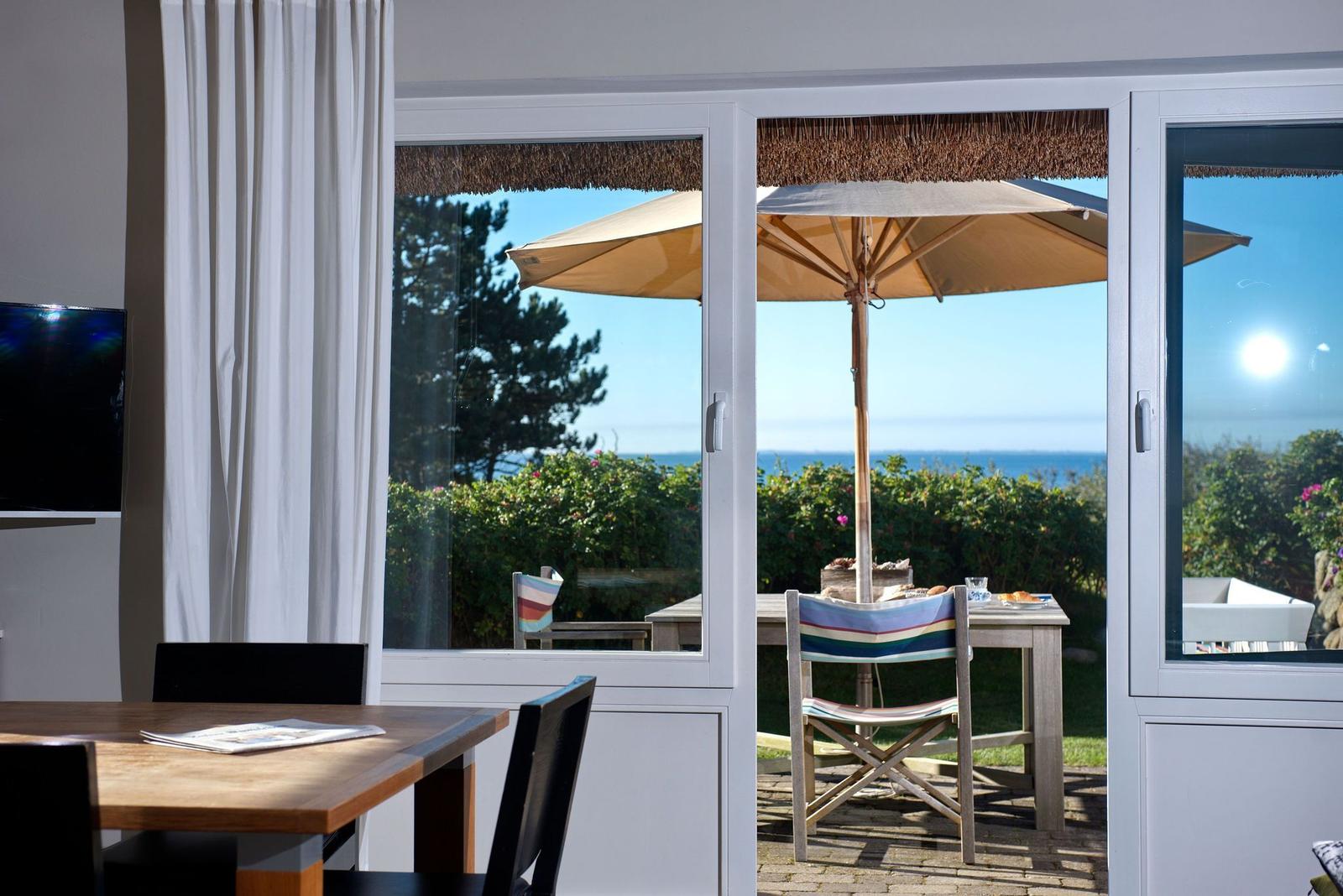 Terrasse mit Tisch, Stühlen und Sonnenschirm. Blick auf Meer und Bäume.