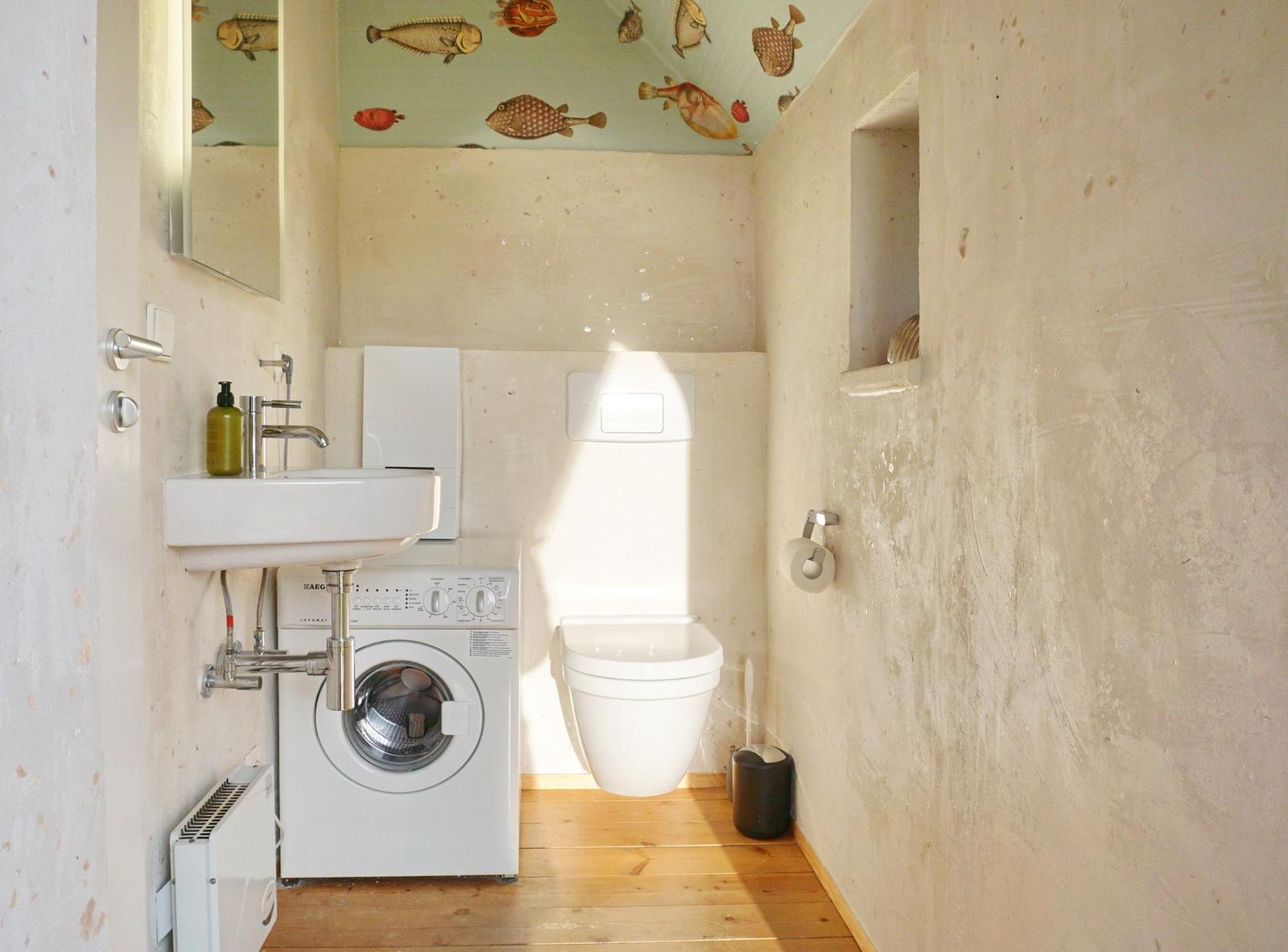 Badezimmer mit Waschmaschine, WC und Fischmotiv an der Decke.