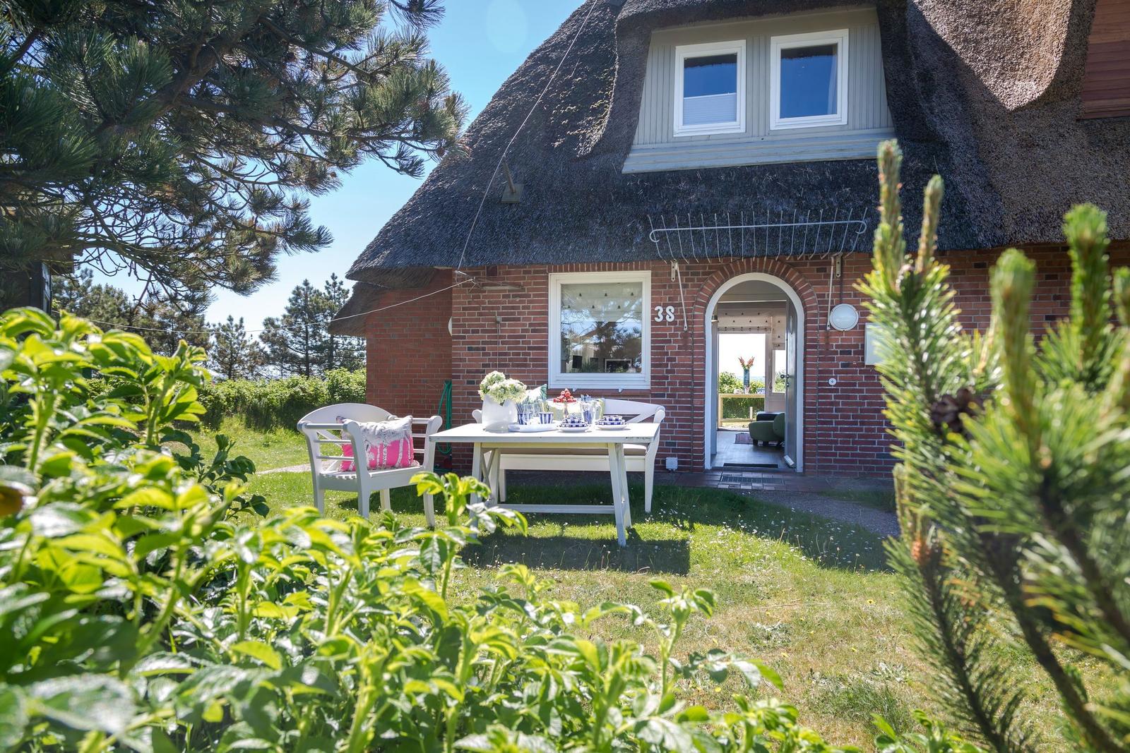 Haus mit Strohdach, weißer Tisch und Stühle im Garten. Tür führt ins Innere.