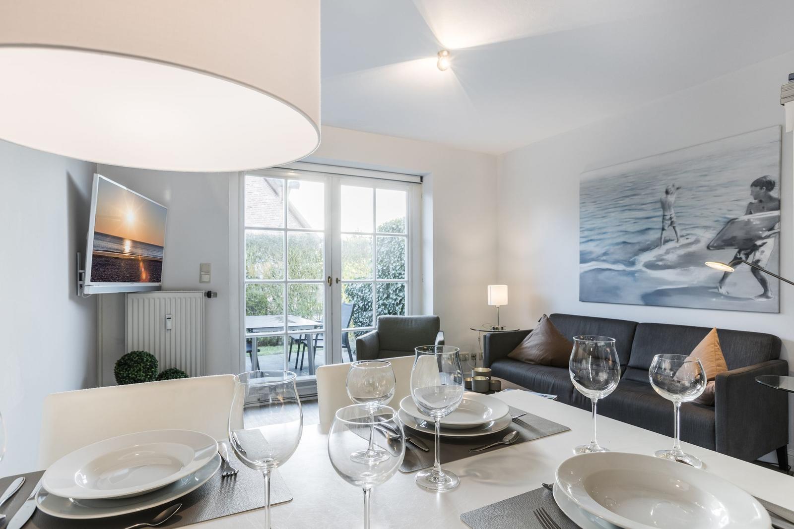 Esstisch mit Gläsern und Teller, Sofa, Fernseher und Fenster zum Garten.