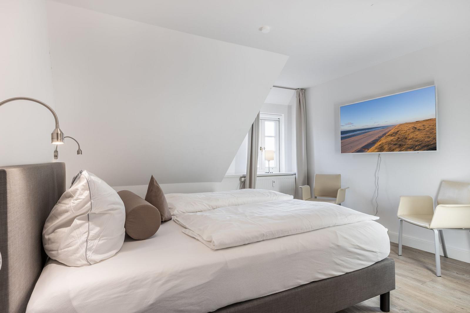 Schlafzimmer mit Doppelbett, Wandbild und Sitzgelegenheiten.