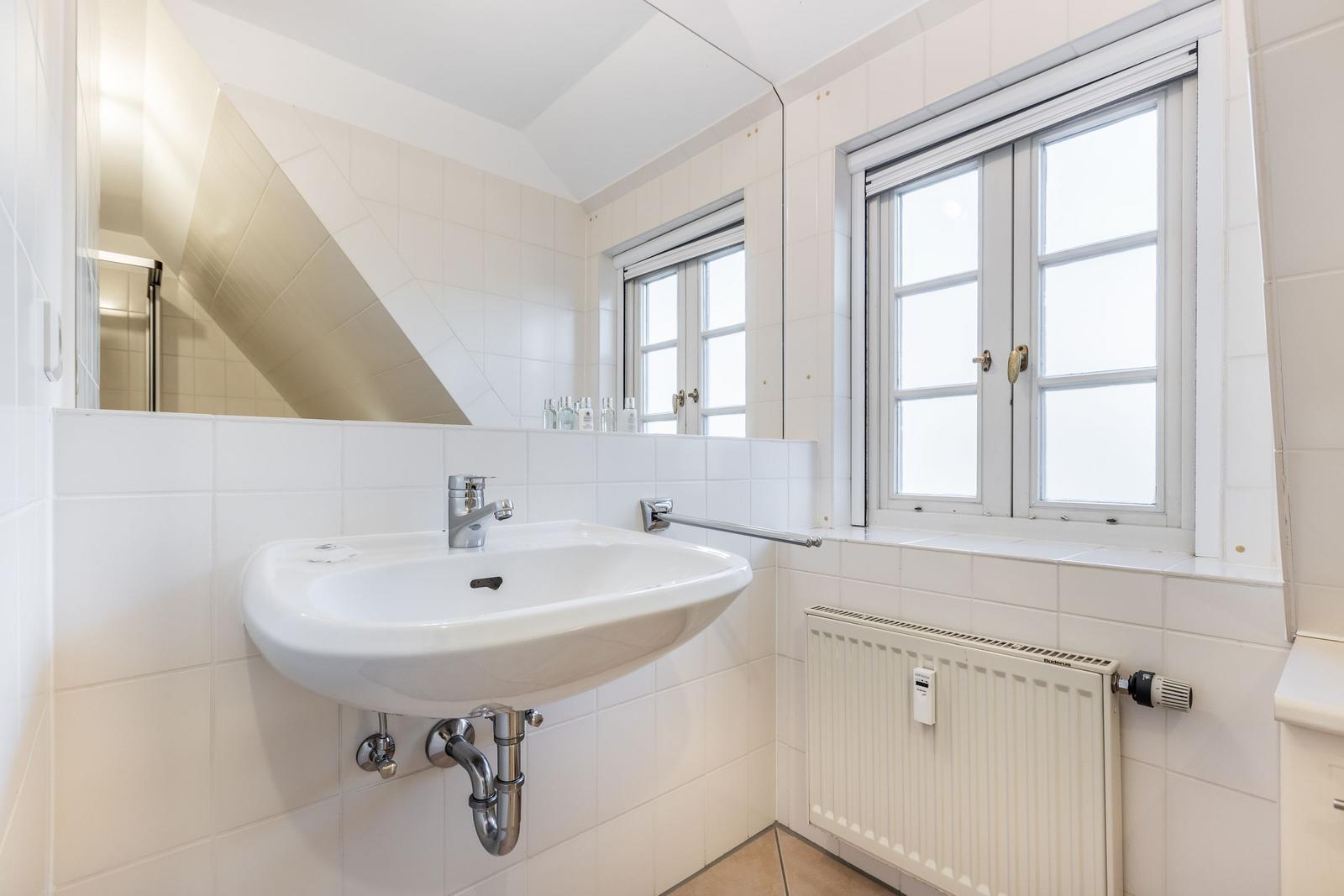 Badezimmer mit Waschbecken, Spiegel und Fenster.
