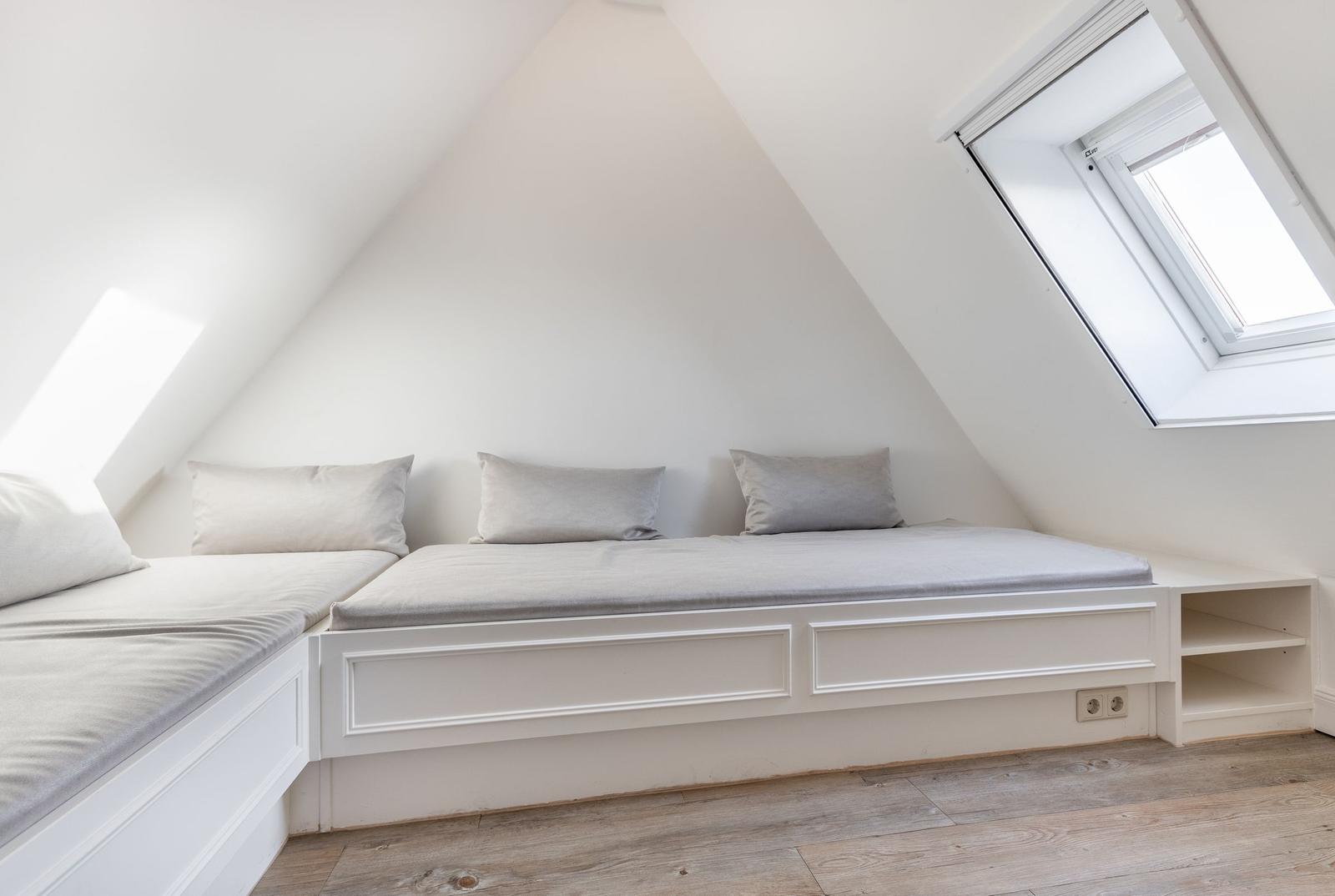 Schlafzimmer mit Dachschrägen, weiße Matratzen und Fenster