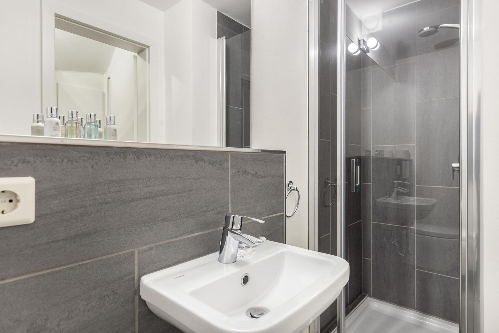 Badezimmer mit Waschbecken, Spiegel und Dusche.