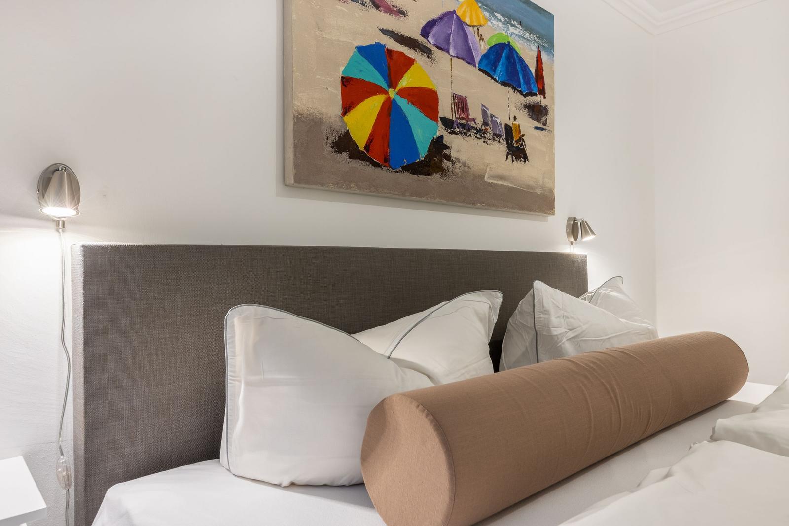 Bettkopfteil mit Kissen und Wandbild mit Strandmotiv.