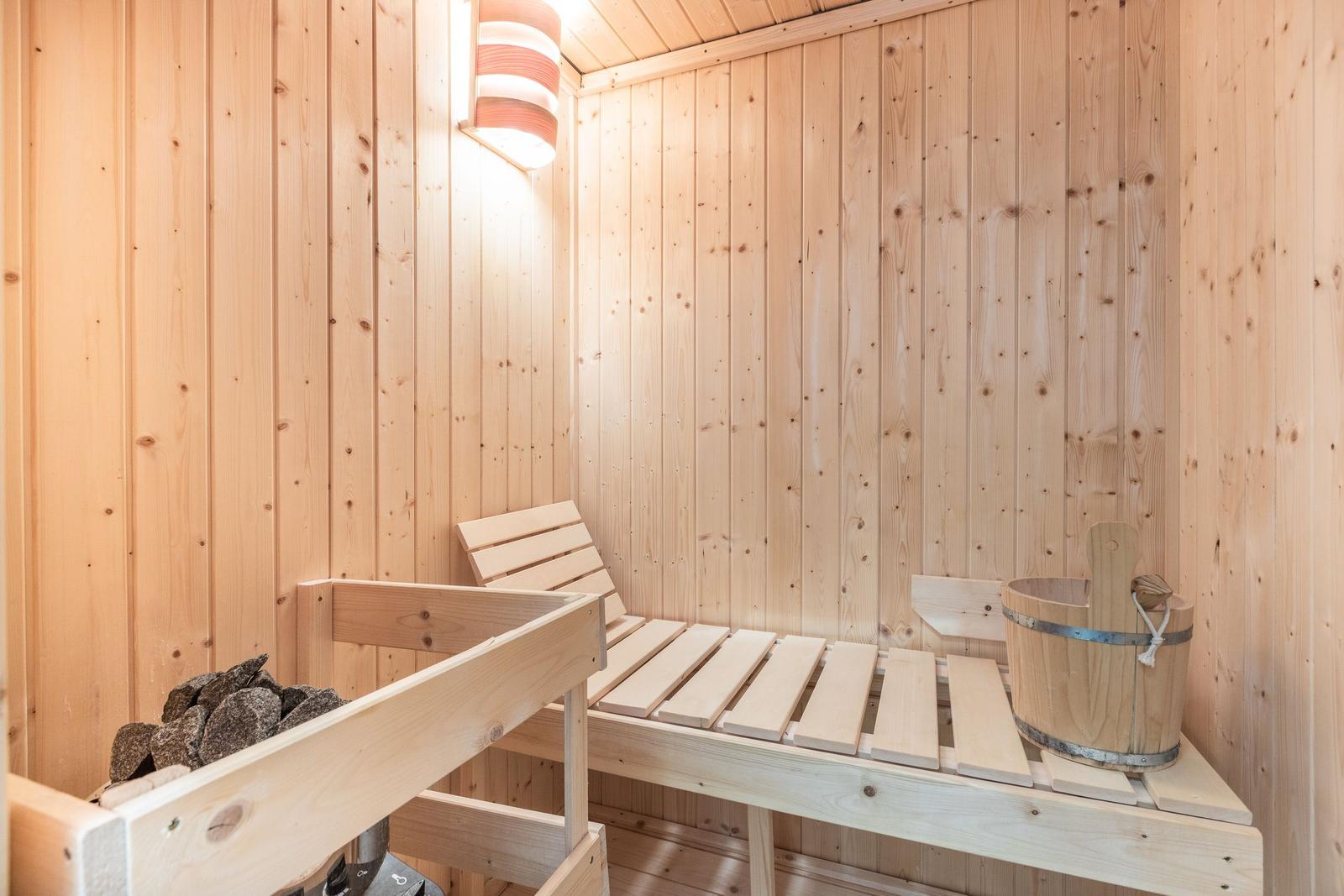 Sauna mit Holzbank, Steinmulde und Eimer.