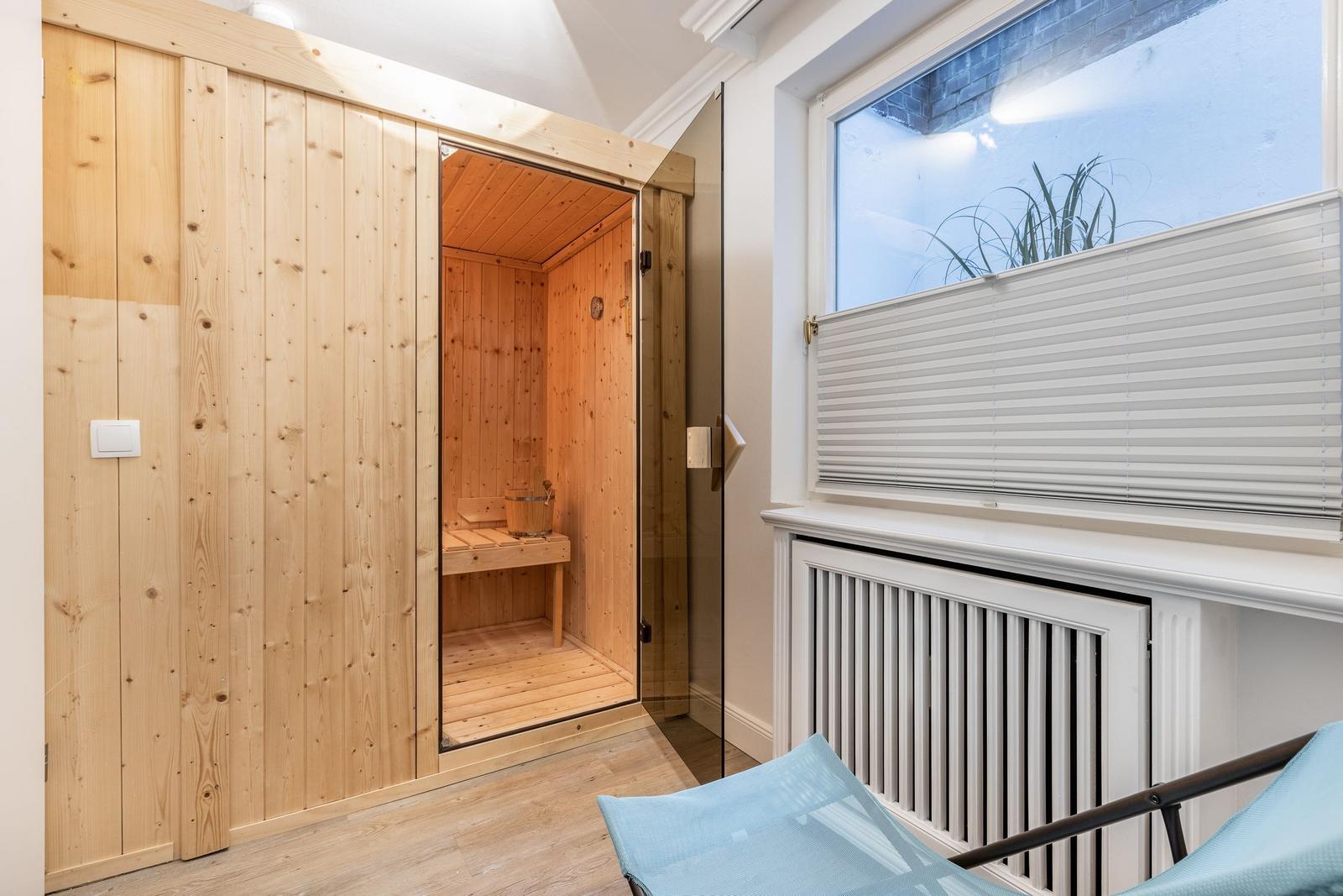 Sauna mit Holzwand und Sitzbank, daneben Fenster mit Jalousie und Liegestuhl.
