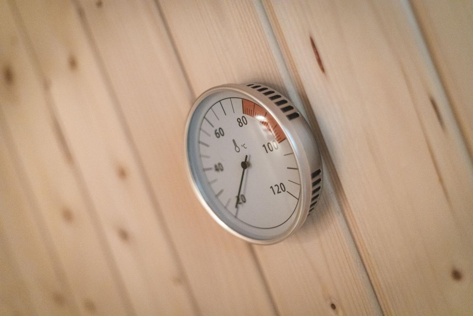 Thermometer an Holzwand in Sauna zeigt Temperatur an.